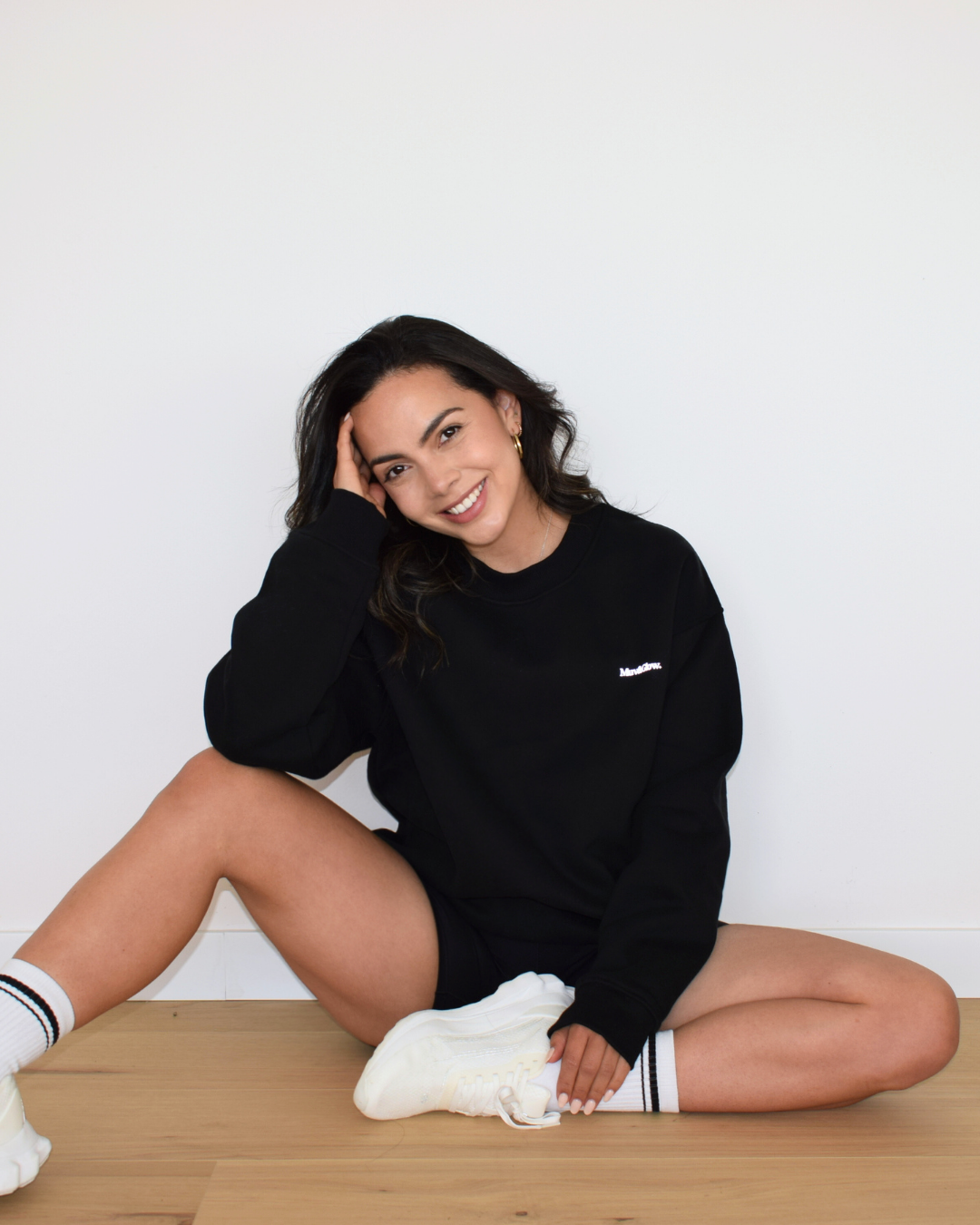 Vista relajada del Essential Pullover negro de Muv&Glow, modelo sentada con sudadera amplia y cómoda.