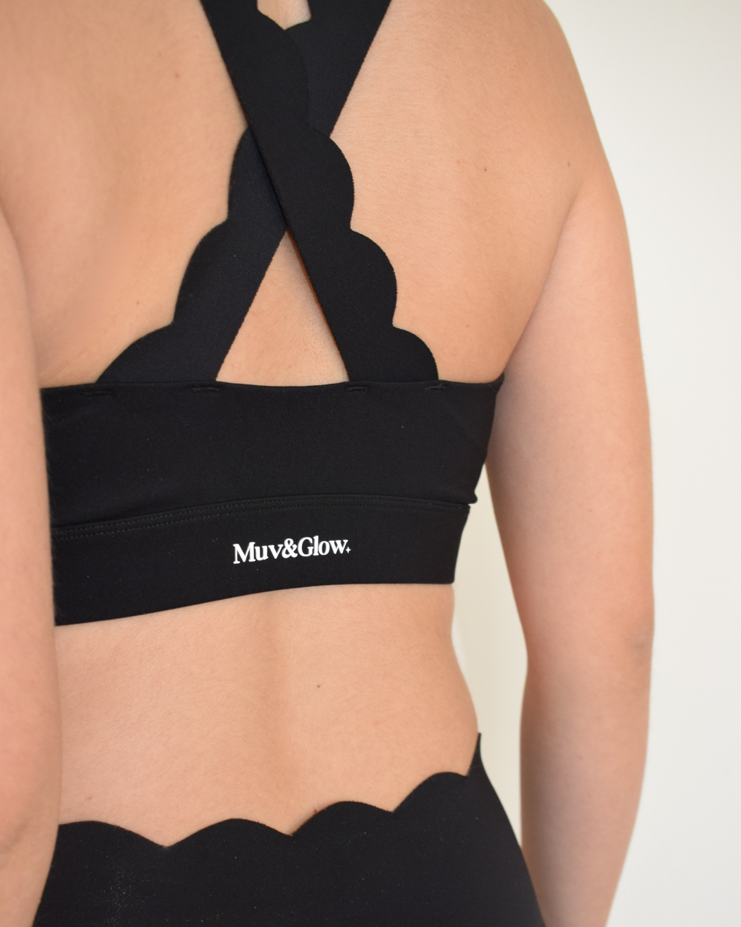 Vista trasera cruzada del top The Edge Bra negro de Muv&Glow mostrando el diseño con tirantes anchos en X.