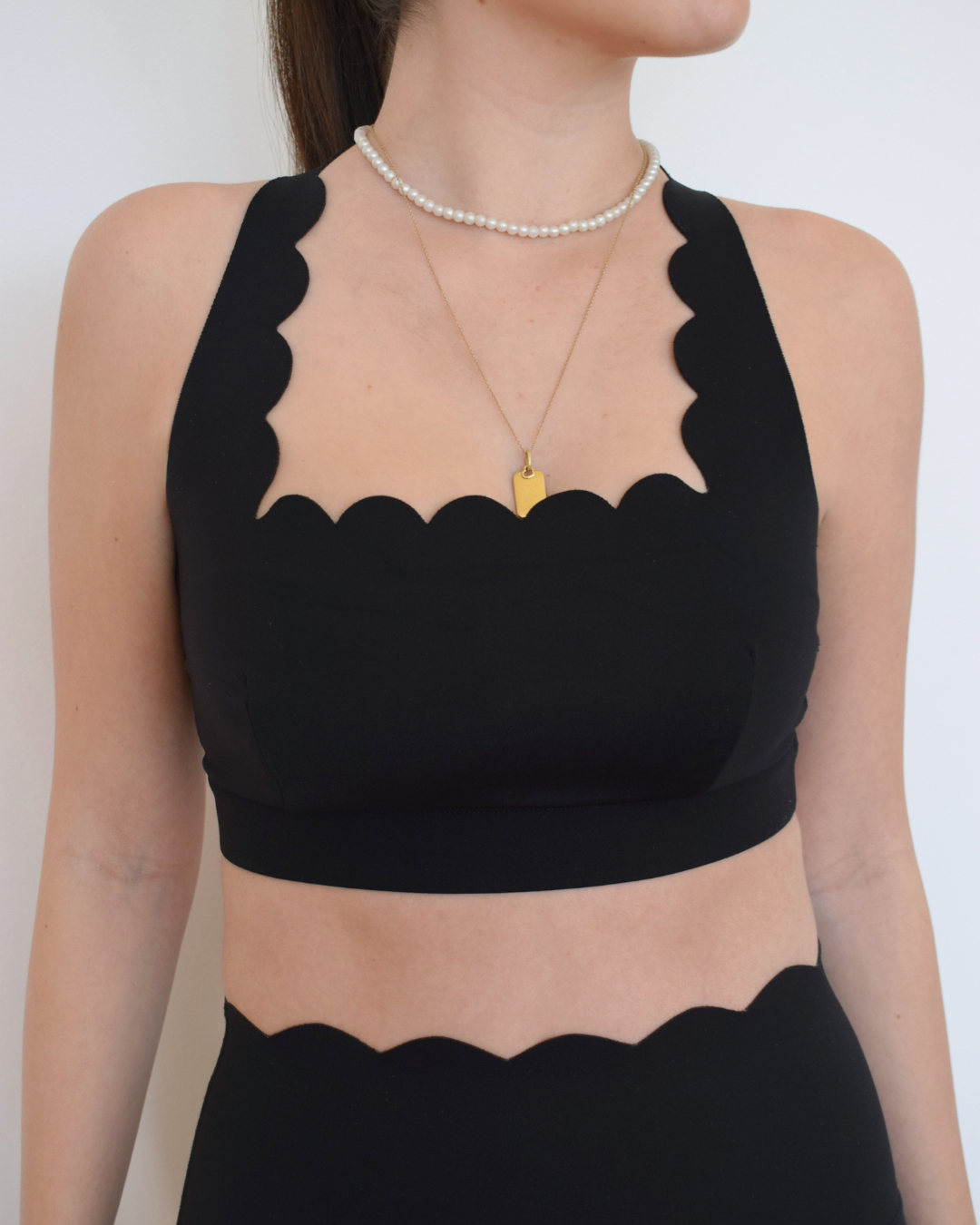 Primer plano del top The Edge Bra negro de Muv&Glow con escote scallop.