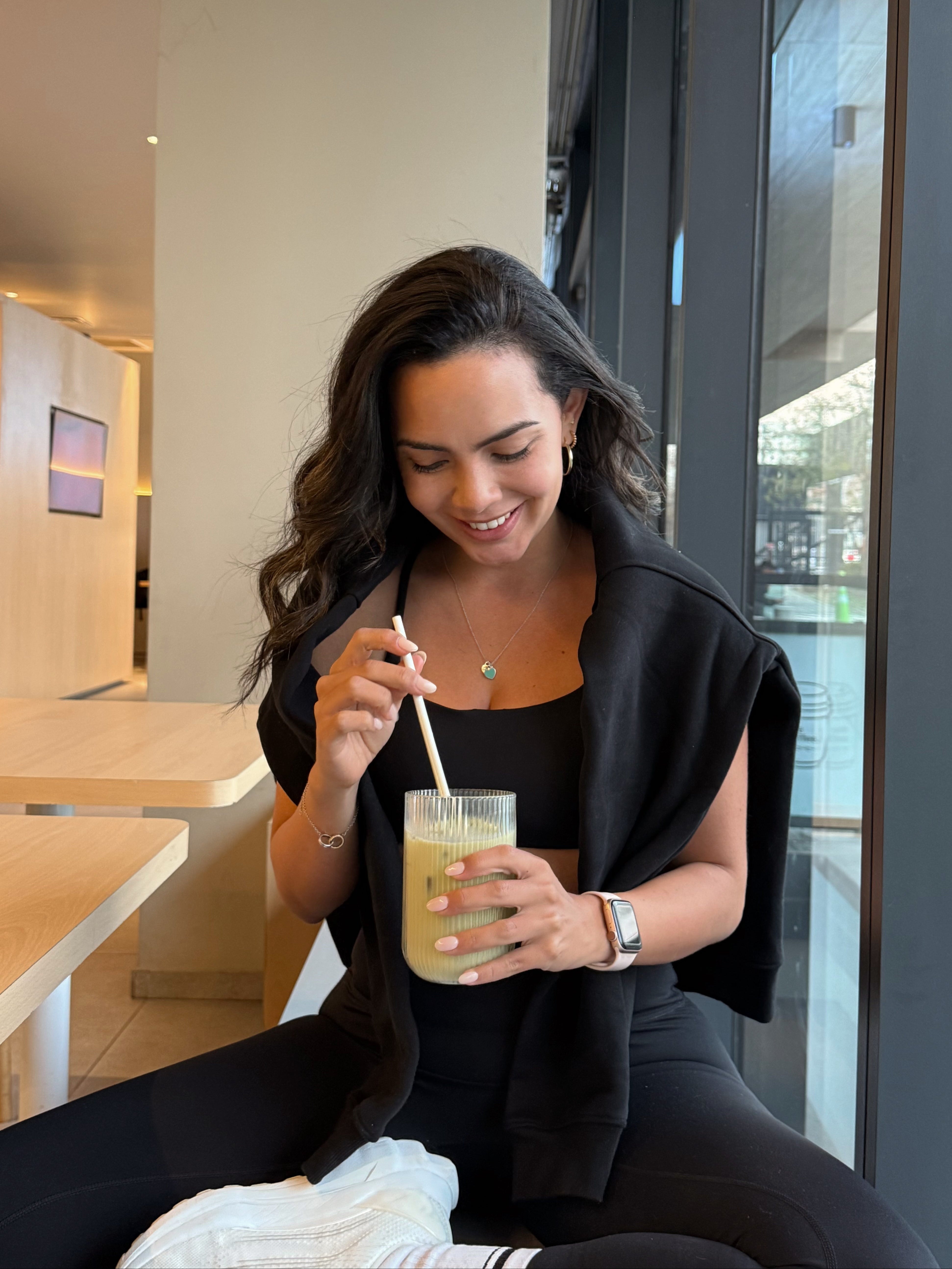 Maria usando el Core Bra y Core Leggings negros de Muv&Glow mientras toma un matcha en una cafetería.