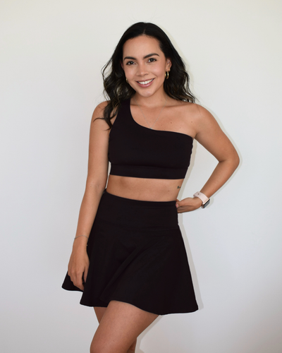 Modelo usando el Core One-Shoulder Bra negro de Muv&Glow, top deportivo minimalista con soporte medio.
