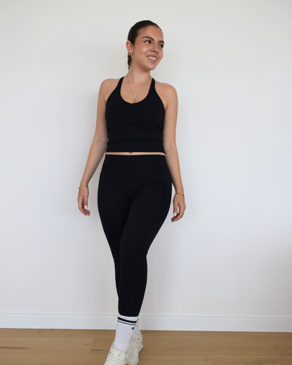 Modelo usando The Core Twist Top negro de Muv&Glow, top largo con escote redondo y soporte medio.