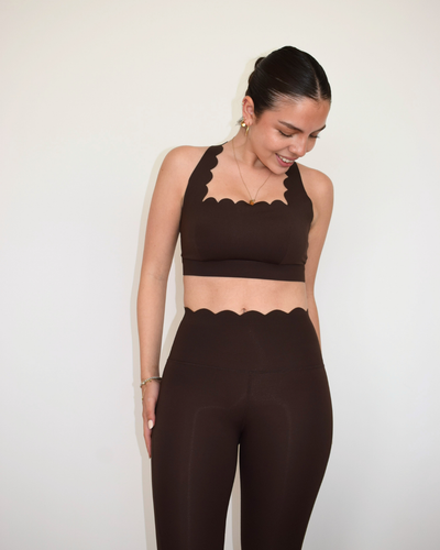 Modelo usando The Edge Bra espresso de Muv&Glow, top deportivo con escote en V y borde ondulado.

