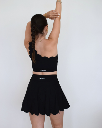 Vista trasera de The Edge Skirt negro de Muv&Glow, short interior cubierto con falda plisada de caída suave.
