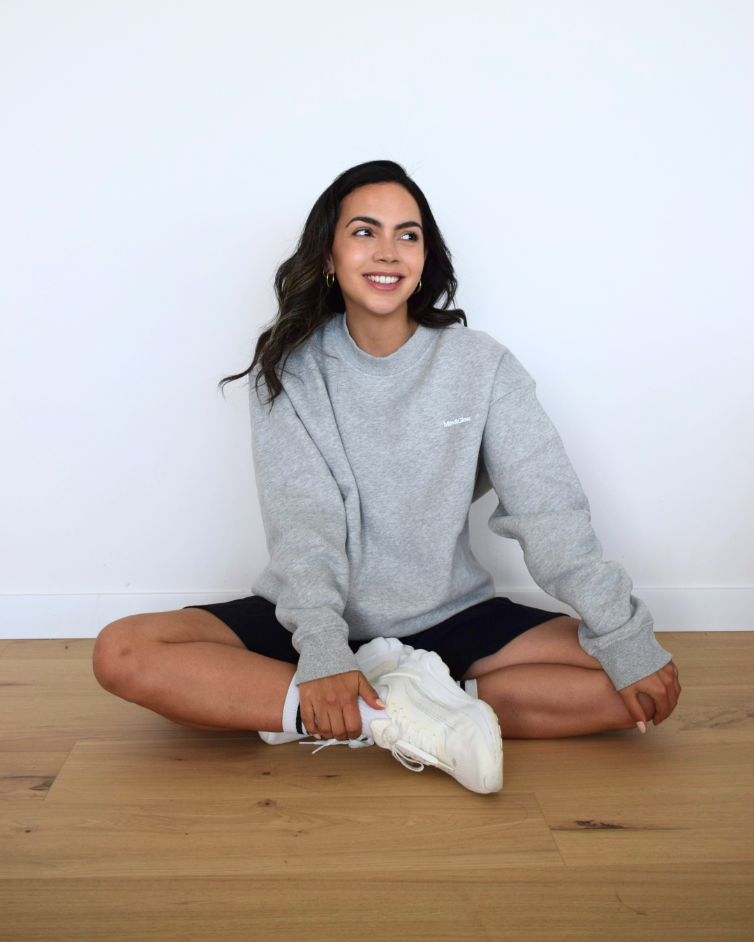 Modelo sentada usando el Essential Pullover gris de Muv&Glow, ideal para descanso o looks casuales.
