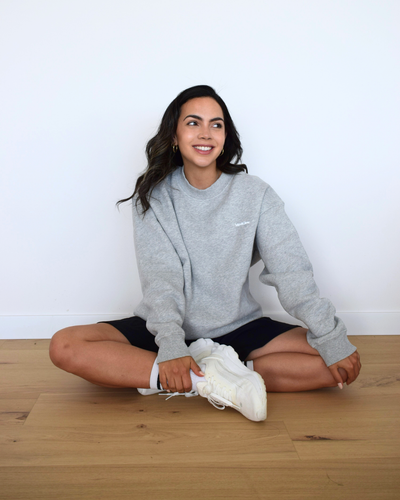 Modelo sentada usando el Essential Pullover gris de Muv&Glow, ideal para descanso o looks casuales.
