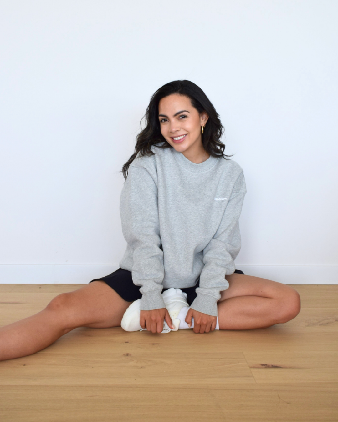 Vista frontal de modelo sentada con el Essential Pullover gris de Muv&Glow, polerón de textura suave y relajada.
