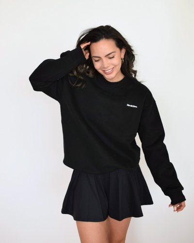 Modelo usando el Essential Pullover negro de Muv&Glow, sudadera oversize perfecta para entrenar o descansar.
