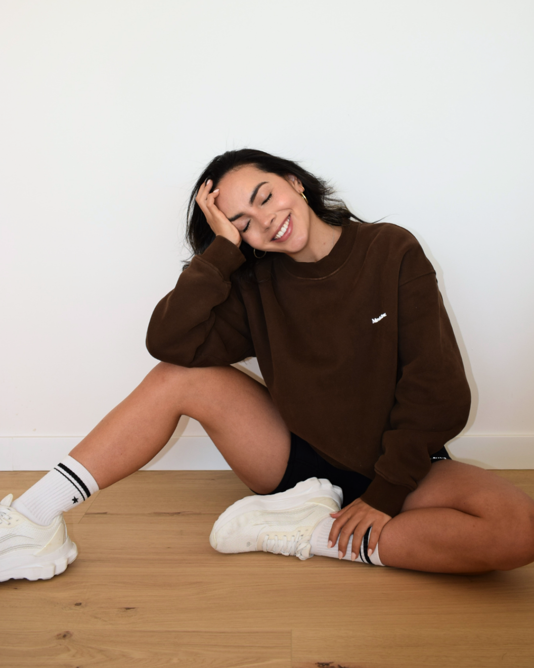 Modelo sonriendo con el pullover espresso, pose relajada en el suelo