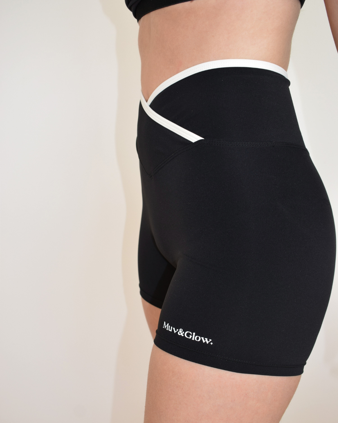 Vista lateral de los Icon Shorts negros con ribete blanco y logo Muv&Glow
