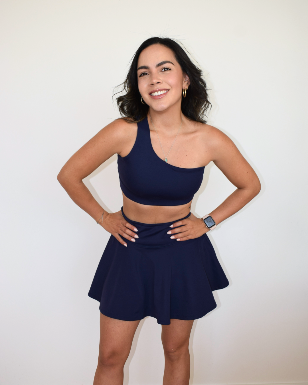 Modelo con conjunto deportivo azul marino Muv&Glow, usando el top Core One-Shoulder y falda.