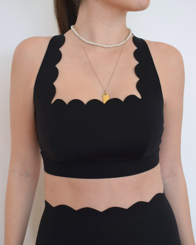 Primer plano del top The Edge Bra negro de Muv&Glow con escote scallop.